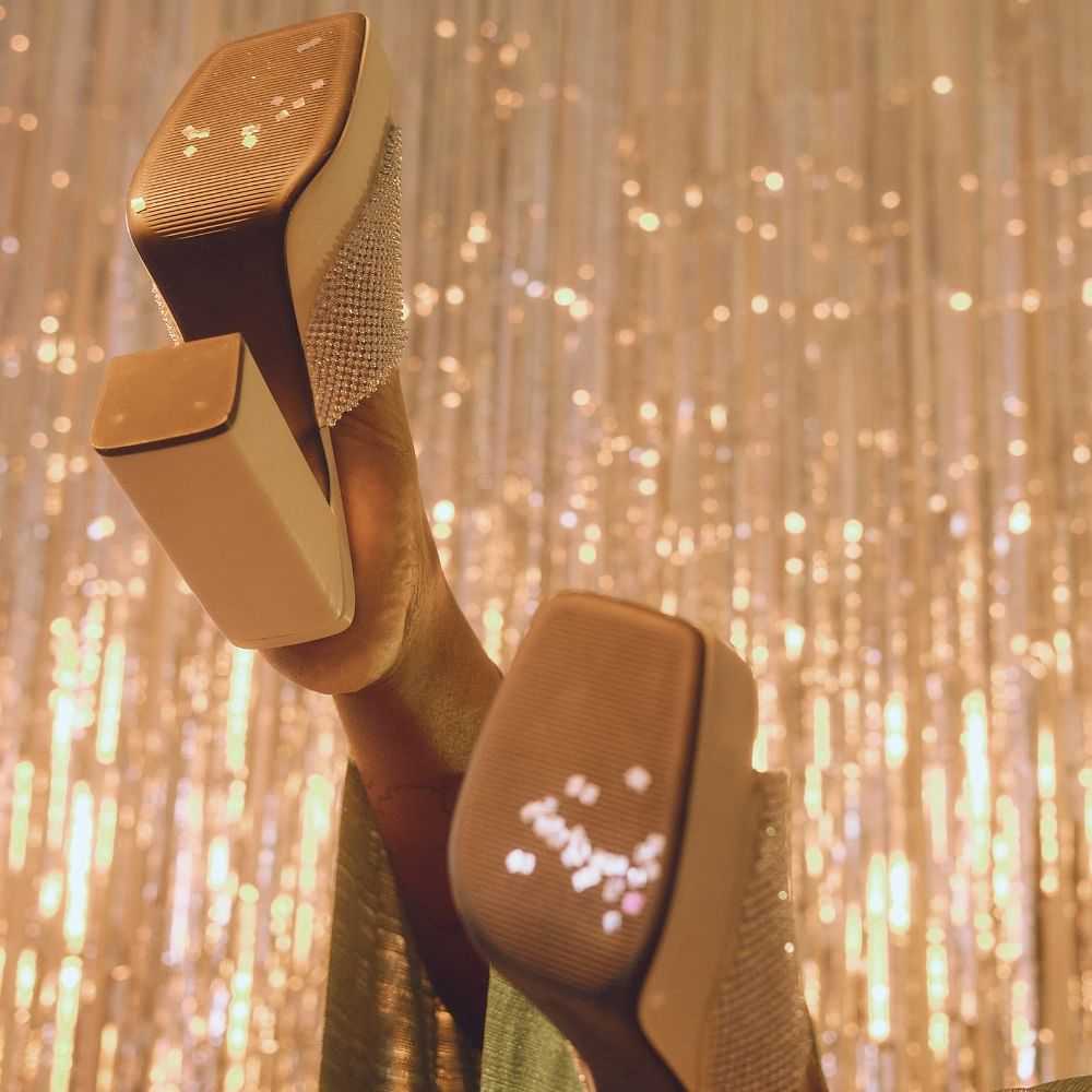 Hand holding sparkling high heels against a glittery backdrop.